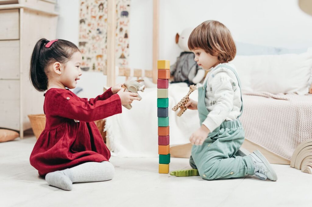 Two young children enjoying playtime with wooden blocks in a cozy indoor setting, fostering creativity and fun.